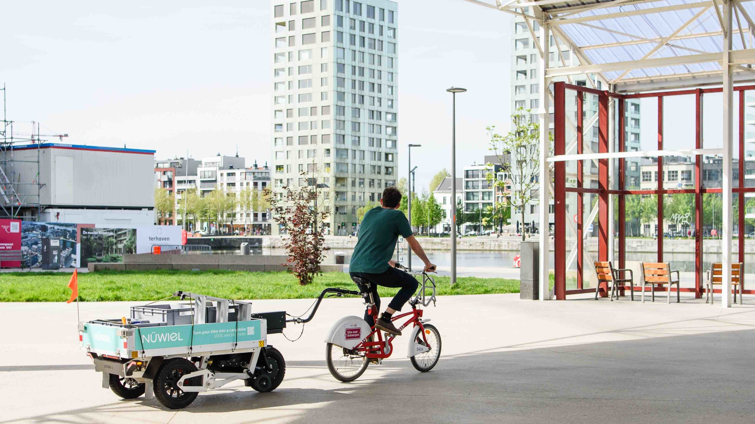 urning a standard bicycle into a high-capacity cargo bike: A NÜWIEL eTrailer in use for urban transport in a modern city district in Antwerp.